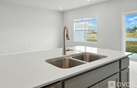 A modern kitchen with a double sink and a window showing a view of a building and a field.