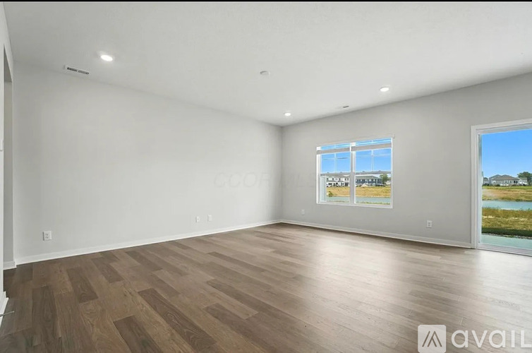 A spacious room with wooden flooring and a large window overlooking a body of water.