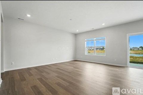 A spacious room with wooden flooring and a large window overlooking a body of water.