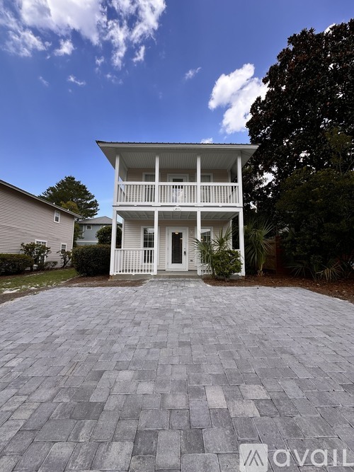 A white two-story house with a balcony and a driveway made of interlocking stones.