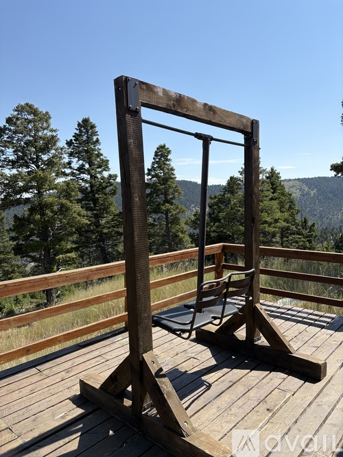 A wooden swing set on a wooden deck with trees in the background.