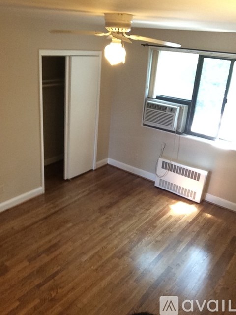 A room with wooden floors and a window with a white air conditioner unit.