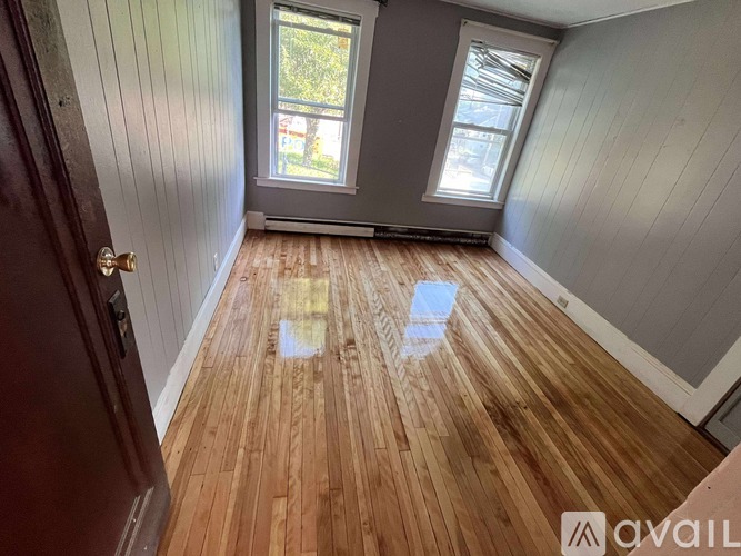 A room with wooden flooring and two windows.