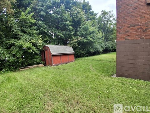 A red shed sits in a grassy field next to a brick wall.