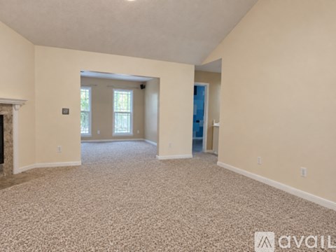 A spacious room with a carpeted floor and a fireplace on the left side.