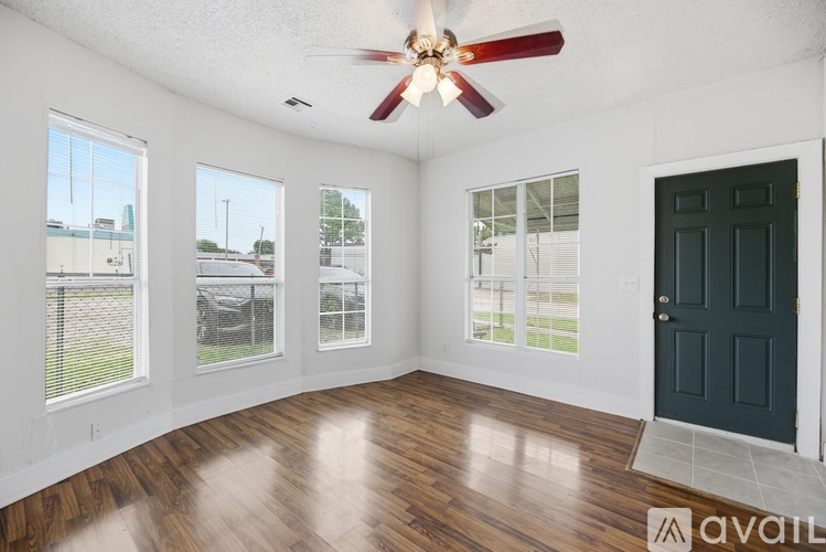 A room with a fan, wooden floor and a black door.
