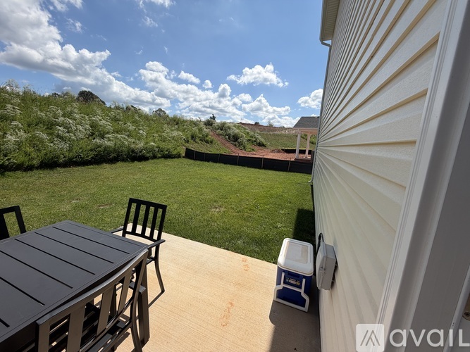 A patio with a table and chairs is shown with a view of a grassy area and a hill in the background.
