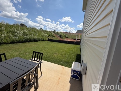 A patio with a table and chairs is shown with a view of a grassy area and a hill in the background.