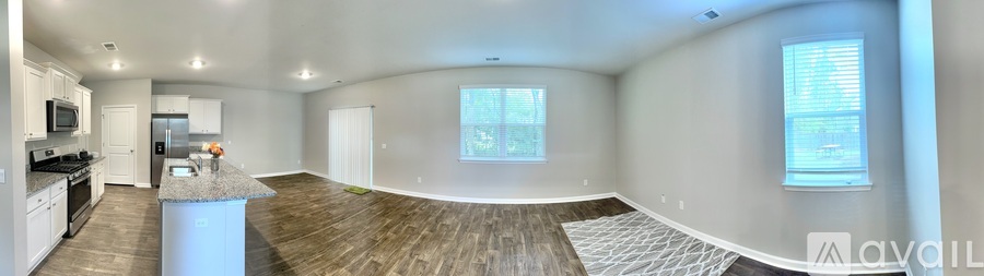 A large, empty living room with wood flooring and a kitchen area in the background.