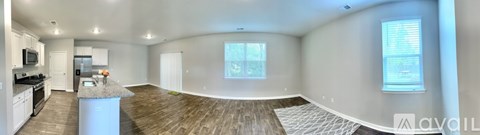 A large, empty living room with wood flooring and a kitchen area in the background.