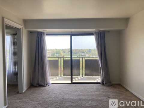 A room with a carpeted floor and a view of a balcony through the window.