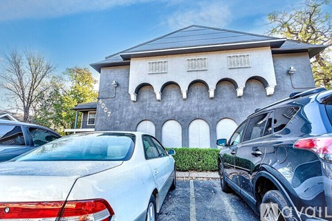 A white car is parked in front of a grey building with a black roof.