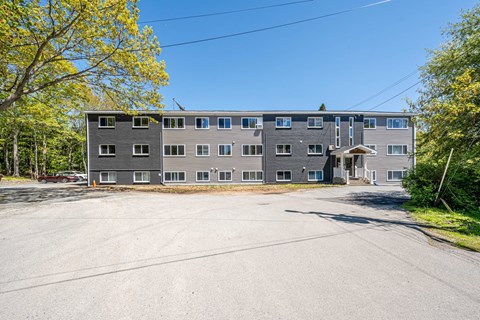 A grey building with a parking lot in front of it.