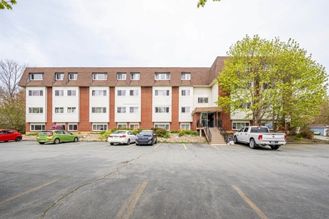 A parking lot in front of a multi-story apartment building with cars parked in the lot.