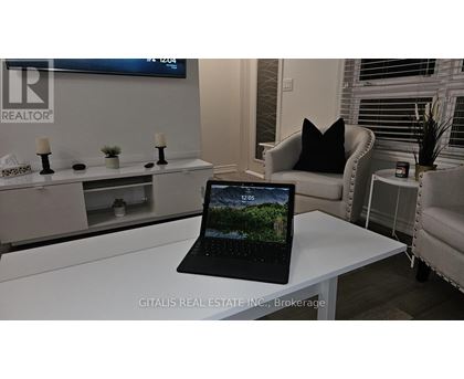 A black laptop is open and displaying a forest scene on a white desk.