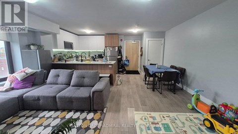 A living room with a grey sofa, a dining table with chairs, and a play area with toys.