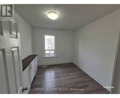 A room with wooden floors and white walls, with a window and a door on the left side.