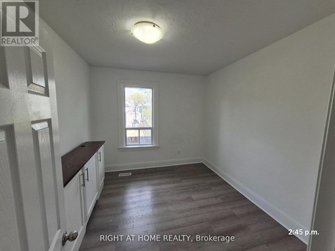 A room with wooden floors and white walls, with a window and a door on the left side.