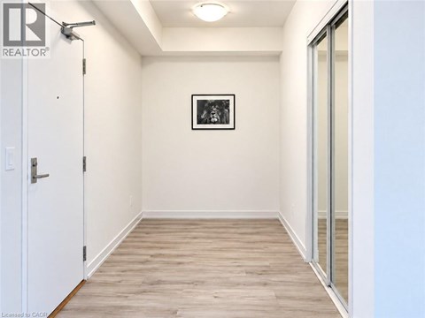 A white door is on the left of a hallway with wood flooring and a picture on the wall.