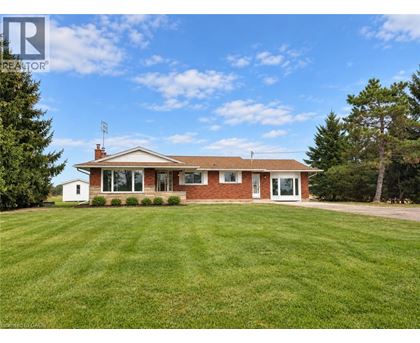 A house with a red brick exterior and a white trim is surrounded by a green lawn.