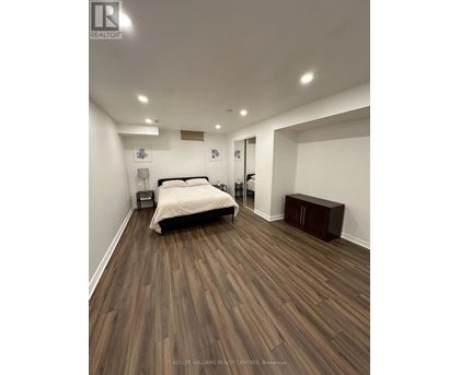 A bedroom with a bed, nightstand, and a wooden floor.