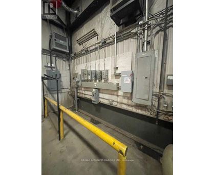 A yellow pole is in the foreground of a room with a wall of electrical boxes.