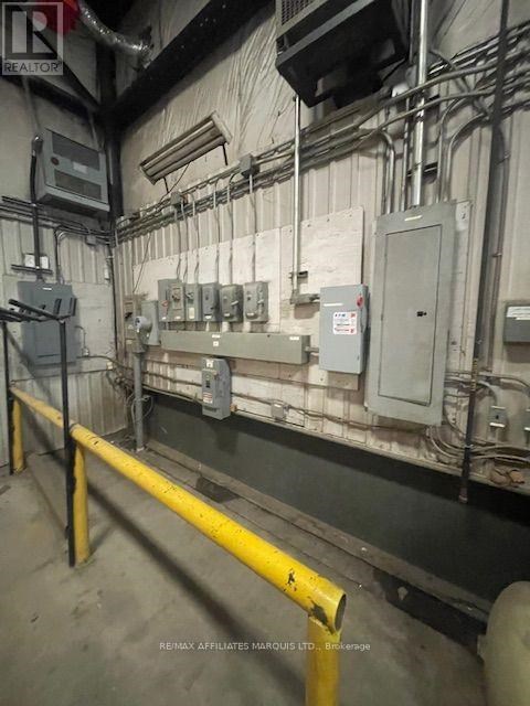 A yellow pole is in the foreground of a room with a wall of electrical boxes.