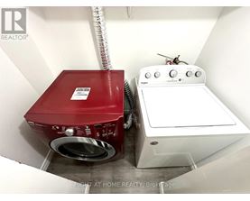 A red washing machine sits next to a white dryer in a small laundry room.