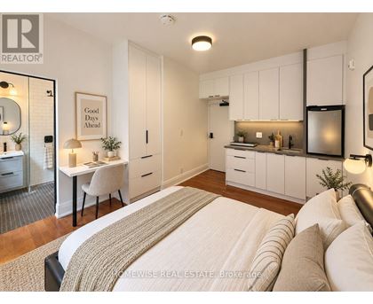 A bedroom with a bed, desk, and kitchen area.