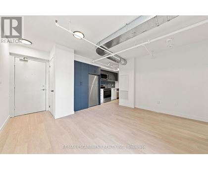 A large empty room with a kitchenette in the background.