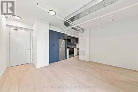 A large empty room with a kitchenette in the background.