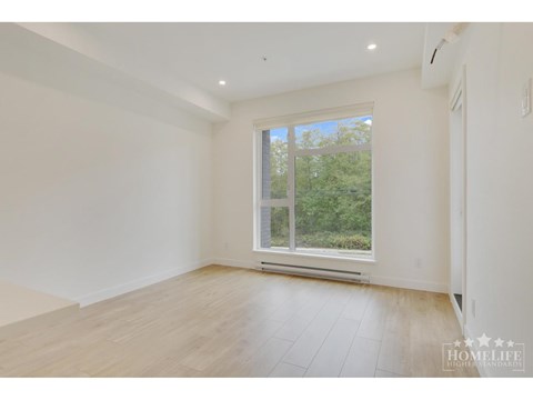 A spacious room with a large window and wooden flooring.