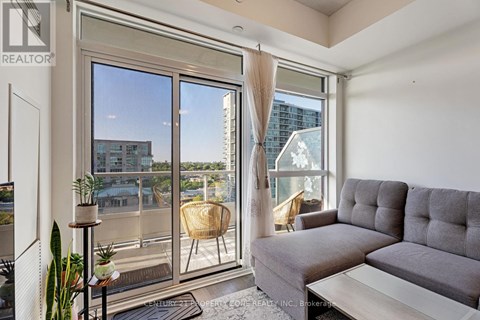 A living room with a grey couch and a large window overlooking a cityscape.