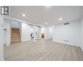 A spacious room with wooden flooring and white walls, with a staircase on the left side.