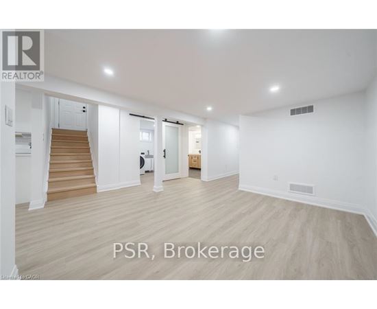 A spacious room with wooden flooring and white walls, with a staircase on the left side.