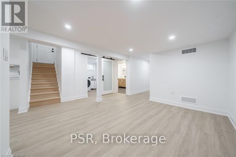 A spacious room with wooden flooring and white walls, with a staircase on the left side.
