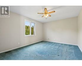 A room with a ceiling fan and a window showing trees outside.