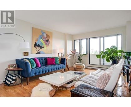A living room with a blue couch and a painting of a woman on the wall.