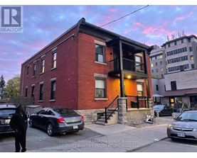 A red brick building with a balcony and cars parked in front.