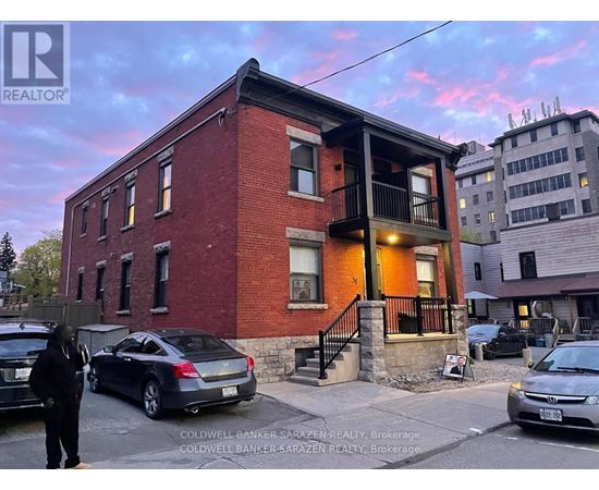 A red brick building with a balcony and cars parked in front.