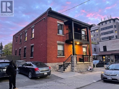A red brick building with a balcony and cars parked in front.