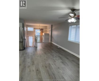 A spacious room with a ceiling fan and light, hardwood floors, and a doorway leading to another room.