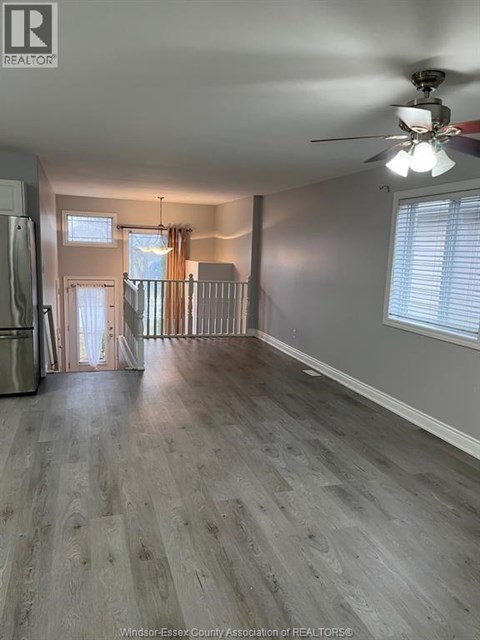 A spacious room with a ceiling fan and light, hardwood floors, and a doorway leading to another room.