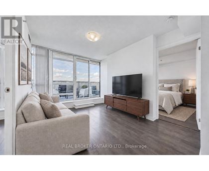 A living room with a couch, a television, and a bed in the background.
