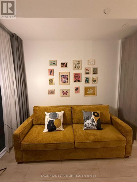A yellow couch with two pillows in front of a wall with pictures on it.