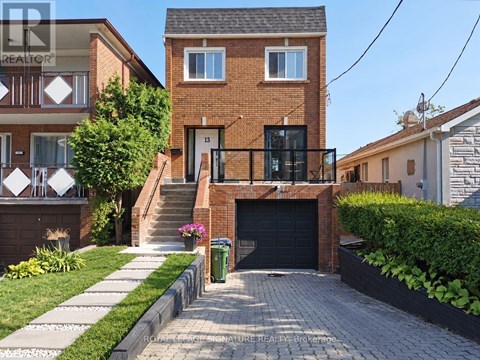 A house with a brick facade and a black garage door is surrounded by a well-kept lawn and a paved driveway.