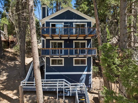 A blue house with a balcony surrounded by trees.