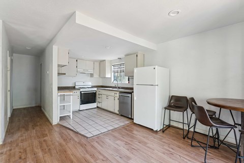 A kitchen with white appliances and brown chairs.