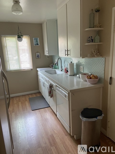 A kitchen with white cabinets and a black trash can.