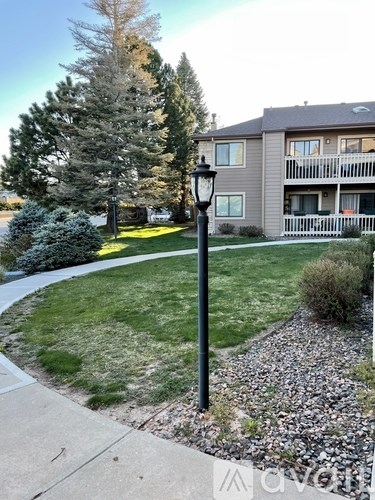 A black lamp post stands on a gravel area in front of a grassy area and a building.